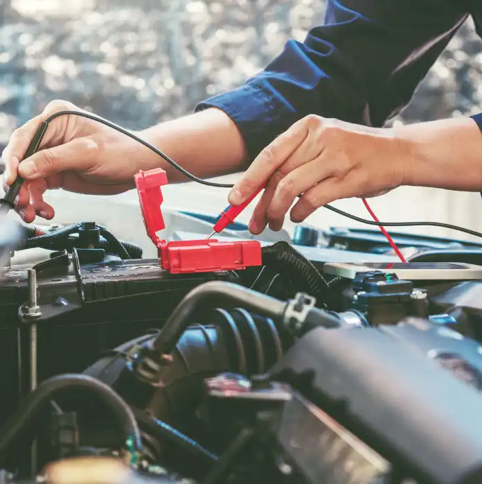 A Man Is Focused On Repairing A Car Battery, Tools In Hand, In A Well-Lit Garage Environment.