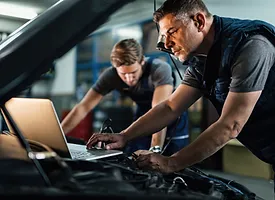 Two Men Collaborating On A Car Repair Inside A Well-Organized Garage, Focused On Their Task With Tools Nearby.