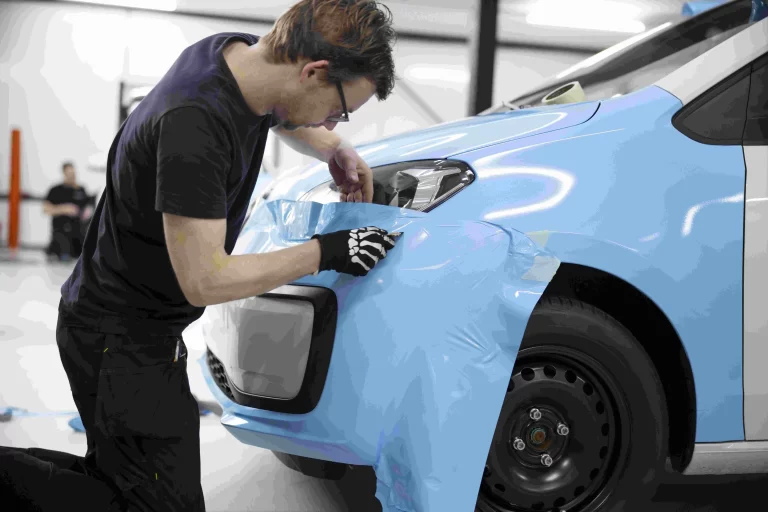 A Man Carefully Paints A Blue Car, Focusing On Details With A Paintbrush In A Well-Lit Garage Setting.